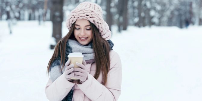 Frau trinkt aus einem Becher im Schnee