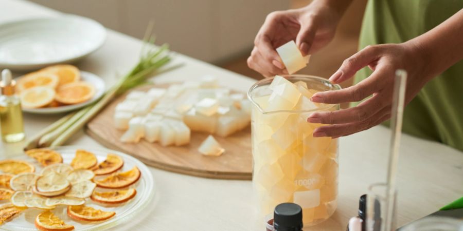 Frau füllt Glas mit Seifenbasis, um es zum Schmelzen zu bringen. Daneben getrocknete Orangenscheiben.