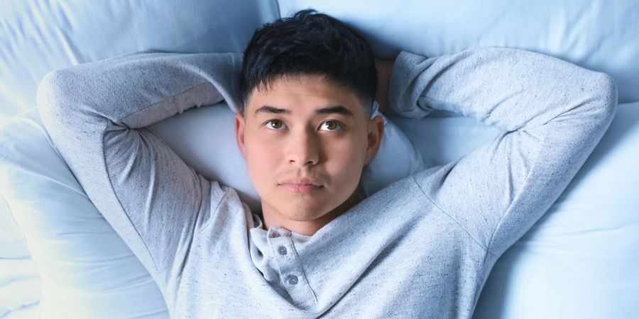 asiatischer mann liegt schlaflos im bett