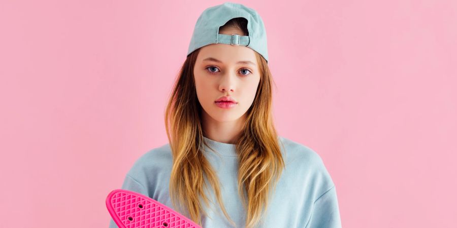 jugendliches blondes mädchen mit rosa skateboard in den händen, rosa hintergrund