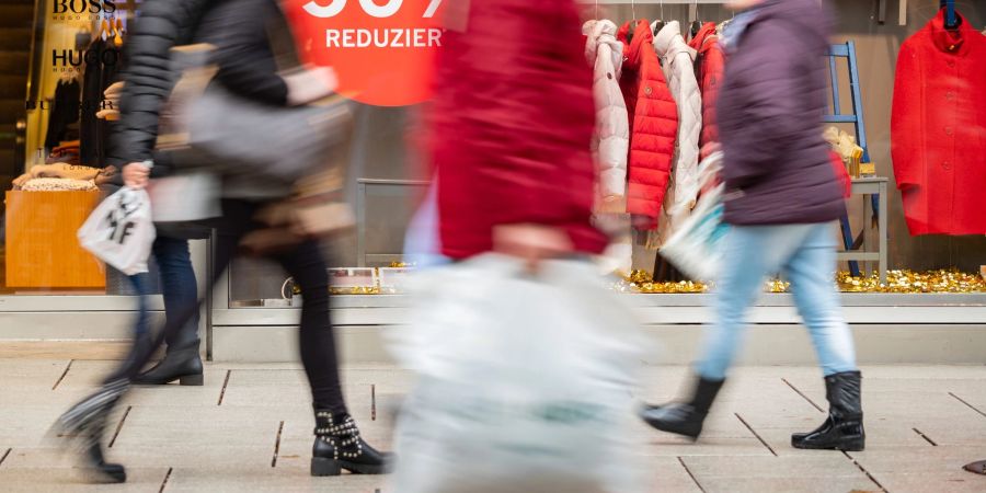 Menschen an einem Rabattschild vorbei. Viele Verbraucher in Deutschland halten sich zu Jahresbeginn aus Skepsis über die wirtschaftliche Entwicklung weiter zurück.