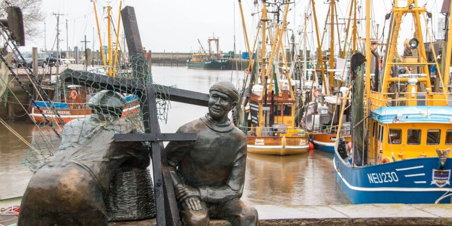 Schwarze Holzkreuze lehnen an der Bronezeskulptur «Alt- und Jungfischer» im Hafen in Neuharlingersiel. Das Fischen mit Grundschleppnetzen steht in der Kritik.