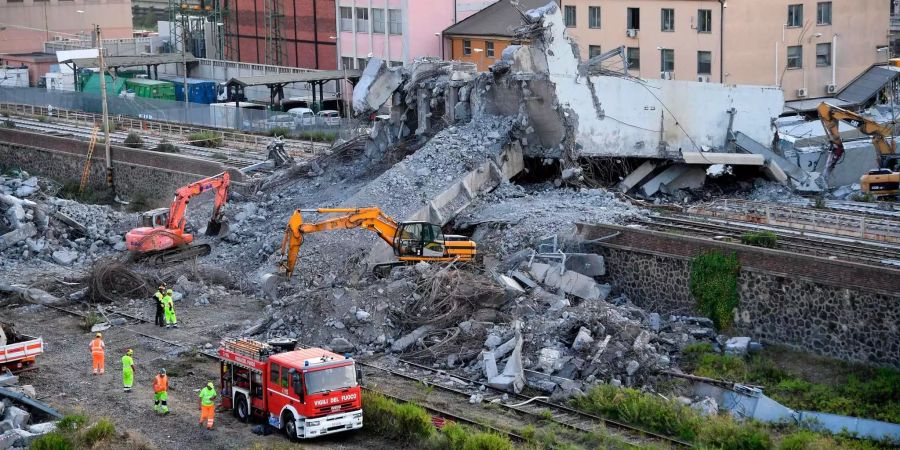 Feuerwehrleute entfernen Trümmer der teilweise eingestürzten Morandi Autobahnbrücke in Genua (IT). In den Trümmern der Brücke wird weiter nach Vermissten gesucht.