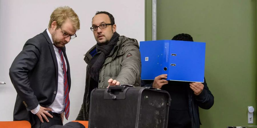 Der Angeklagte hält sich einen Ordner vors Gesicht.