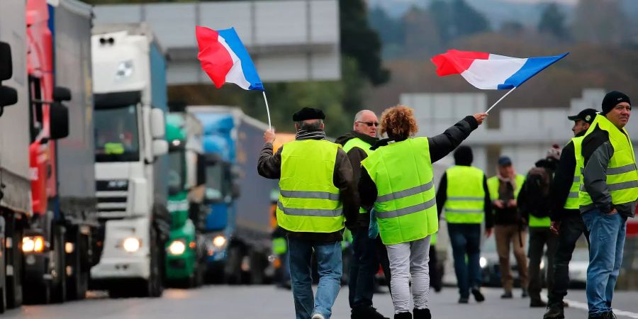 Demonstranten schwenken französische Flaggen, während sie Lastwagen auf der Autobahn blockieren.