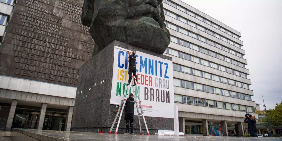 Zwei Männer befestigen am Karl-Marx-Denkmal ein Plakat mit der Aufschrift «Chemnitz ist weder grau noch braun».