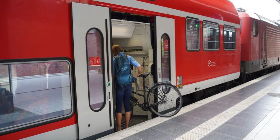 Eine Reisende steigt mit ihrem Fahrrad in eine Regionalbahn Richtung Rostock.