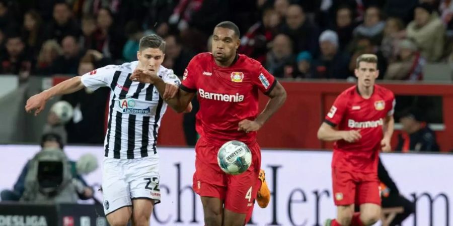 Leverkusens Jonathan Tah (M) und Freiburgs Roland Sallai kämpfen um den Ball. Foto: Bernd Thissen/dpa