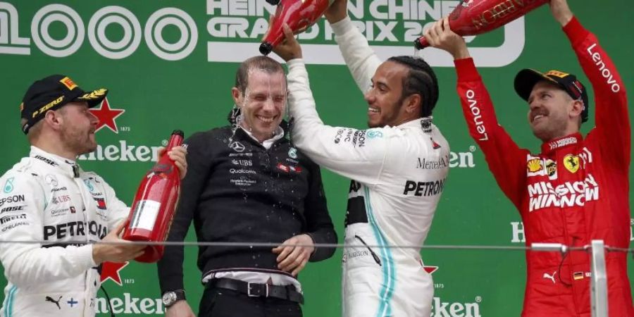 Sebastian Vettel (r) spendiert für Sieger Lewis Hamilton eine Champagner-Dusche. Foto: Andy Wong/AP