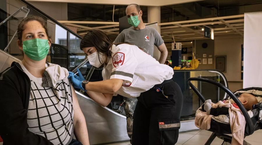 Ein israelischer Sanitäter des medizinischen Dienstes Magen David Adom (r) injiziert einer Frau eine Corona-Impfdosis in einer Ikea-Filiale in Rishon Lezion.