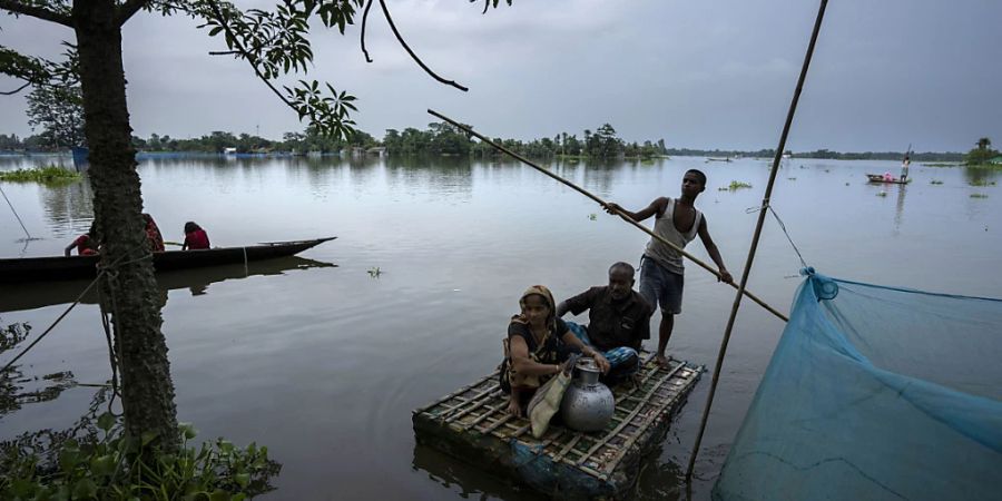 Von der Überschwemmung betroffene Menschen erreichen mit einem Behelfsboot ein sichereres und höher gelegenes Gebiet im Dorf Tarabari. Foto: Anupam Nath/AP/dpa