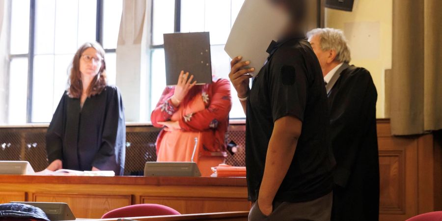 Die beiden Angeklagten verdecken im Gerichtssaal vor Sitzungsbeginn in Tübingen ihre Gesichter.