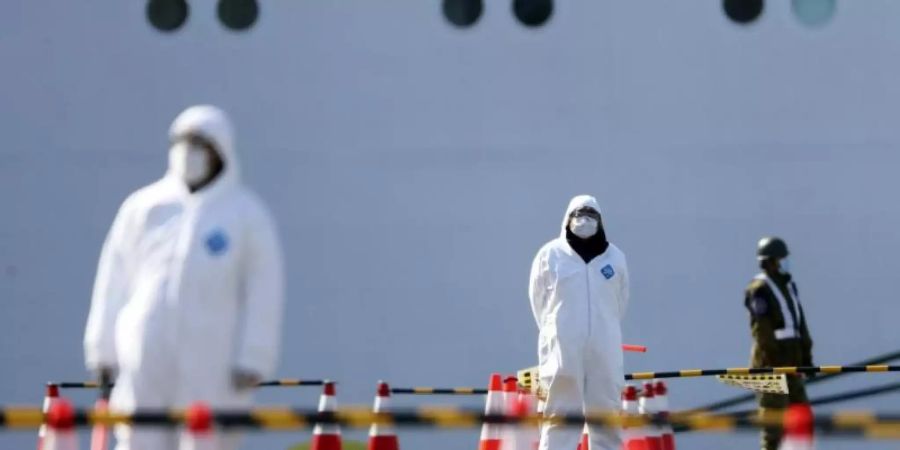 Sicherheitskräfte stehen vor der «Diamond Princess». Das Schiff hatte wegen des neuartigen Coronavirus Sars-CoV-2 zwei Wochen lang im japanischen Yokohama unter Quarantäne gestanden. Foto: Eugene Hoshiko/AP/dpa