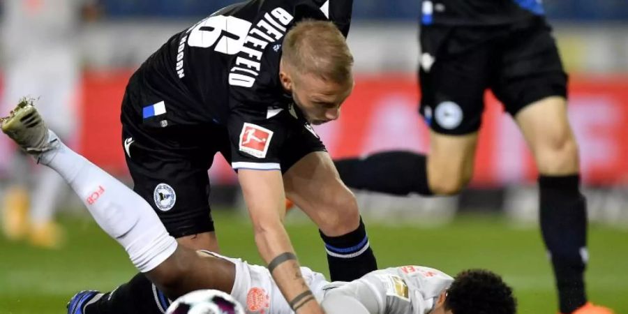 Bayern Münchens Serge Gnabry (unten) im Zweikampf mit dem Bielefelder Mike van der Hoorn. Foto: Martin Meissner/AP-Pool/dpa