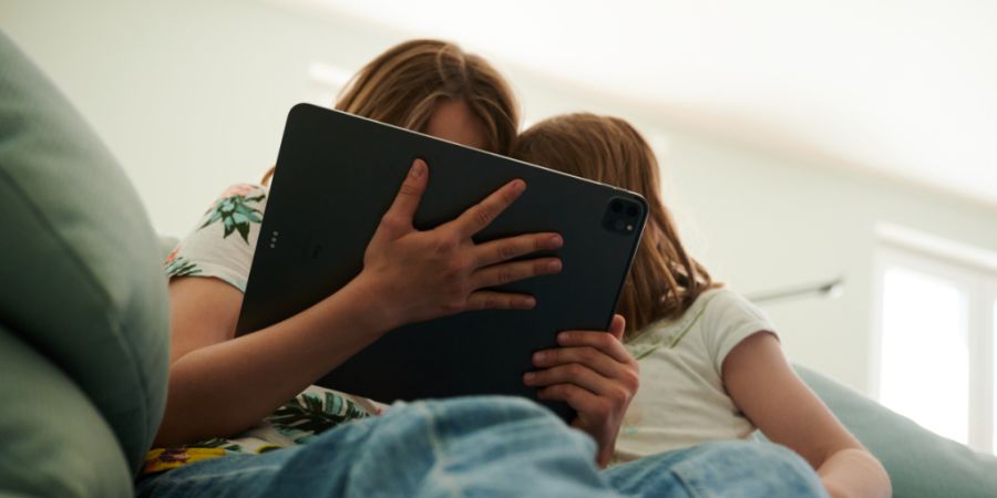 ARCHIV - Zwei Schwestern sitzen auf der Couch und gucken in das Tablet ihrer Eltern. Foto: Annette Riedl/dpa/Symbolbild