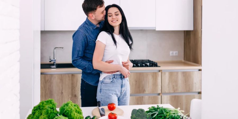 Ehepaar steht kuschelnd in der Küche und kocht