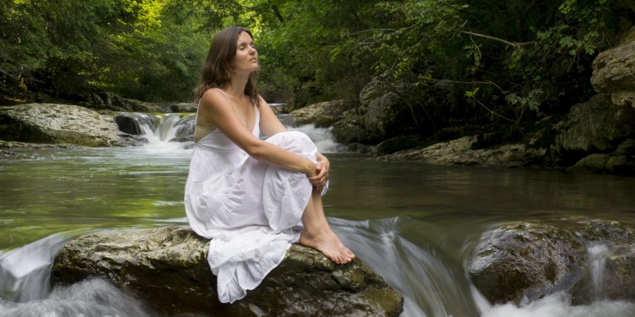 frau sitzt in weissem kleid auf stein in fluss