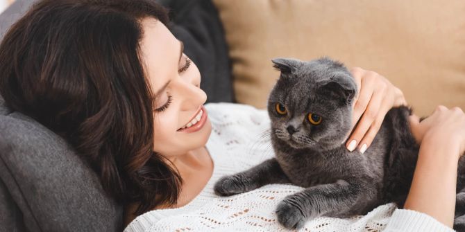 Frau mit grauer Katze auf dem Bauch.