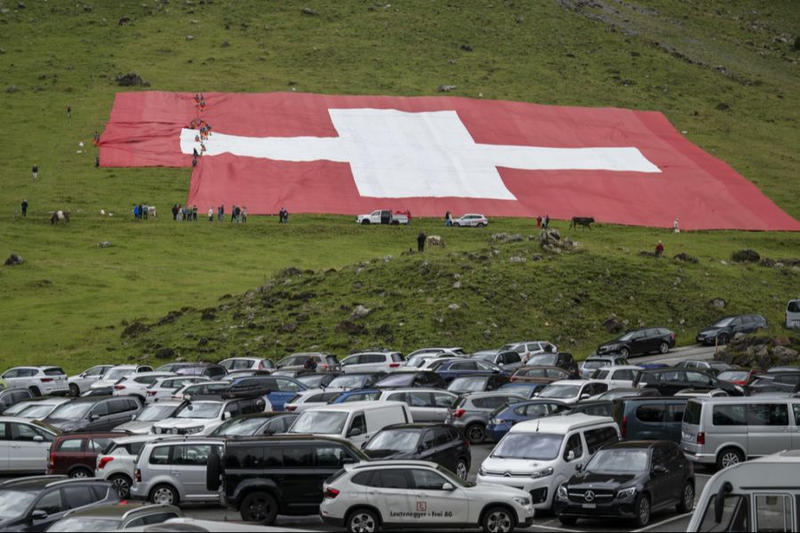 Eine überdimensionierte Schweizerfahne ist am Donnerstag nach dem Ausrollen an einem Wiesenhang am Fusse des Säntis zerrissen.