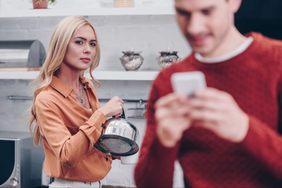Mann mit Smartphone wird von Frau im Hintergrund beobachtet