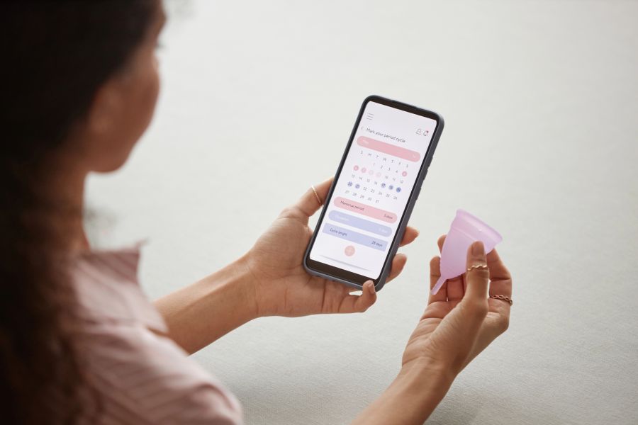 Frau mit Periodentasse und Zyklus-App
