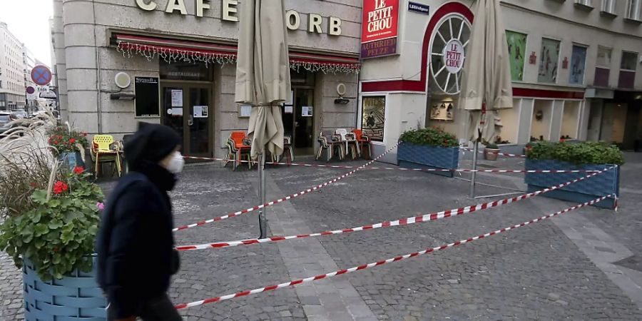 Ein Mann mit Mund-Nasen-Schutz geht an einem geschlossenen Cafe in der Innenstadt vorbei. In Österreich sind seit Anfang November wegen der drohenden Überfüllung der Intensivstationen in der Corona-Pandemie Kultur, Gastronomie und Freizeiteinrichtungen geschlossen, seit Mitte November auch Schulen und die meisten Geschäfte. Foto: Ronald Zak/AP/dpa