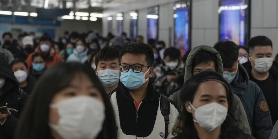 Pendler mit Schutzmasken gehen während des morgendlichen Berufsverkehrs auf dem Weg zur Arbeit in Peking durch einen Gang zwischen zwei U-Bahn-Stationen. China passt sich weiter an die Lockerung der strengen Vorschriften zur Eindämmung des Virus an. Foto: Andy Wong/AP/dpa