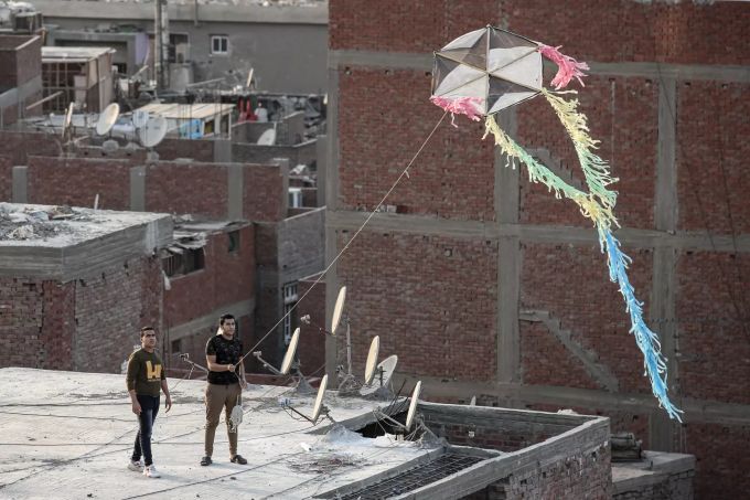 Zwei Männer lassen einen handgemachten Drachen über Wohngebäude im Al Munib-Viertel fliegen. Drachensteigen in Ägypten