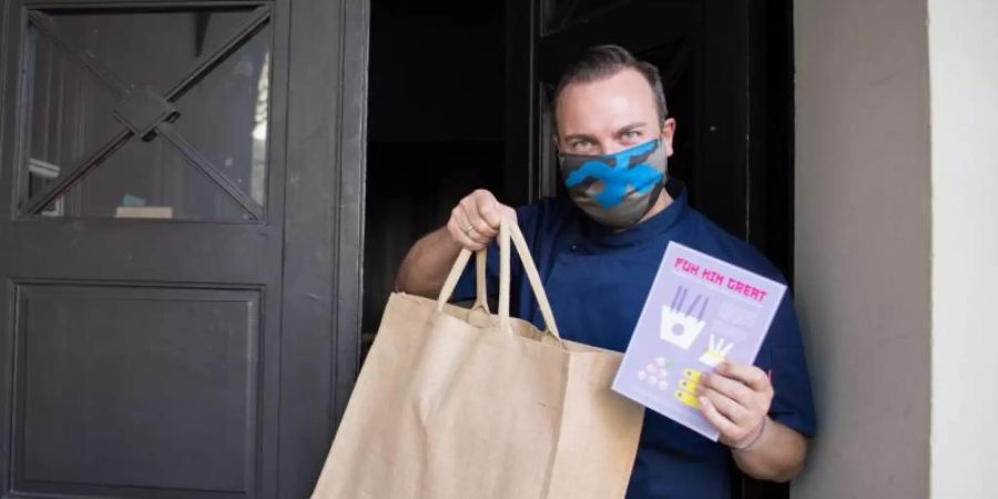 Zwei-Sterne-Koch Tim Raue hält Essen in einer Tragetasche und eine Speisekarte in den Händen. Wegen des Coronavirus bietet Raue nun auch einen Lieferservice für sein Essen an. Foto: Jörg Carstensen/dpa