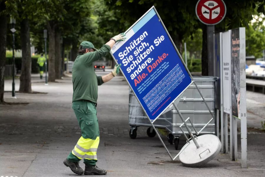 Ein Mitarbeiter der Stadtgärtnerei entfernt ein Schild, das zur Achtung wegen des Coronavirus mahnen soll.