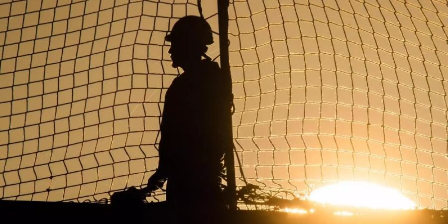 Ein Bauarbeiter bei Sonnenaufgang auf einer Baustelle auf dem Dach einer Gewerbehalle. Foto: Julian Stratenschulte/dpa