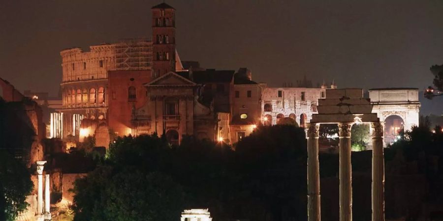 Das Forum Romanum in Rom wird von Strahlern beleuchtet. Dahinter steht das Colosseum.