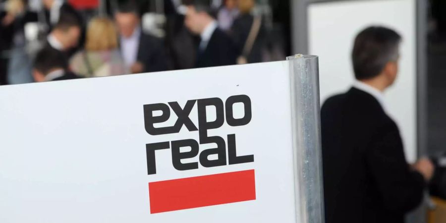 Besucher kommen zur Messe expo real und gehen an einem Logo der Messe vorbei.