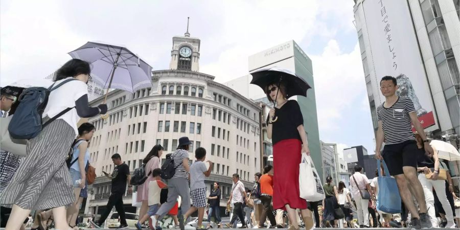 Zwei Japanerinnen mit Sonnenschirmen überqueren eine mit Menschen bevölkerte Strasse des Einkaufsviertels Ginza in Tokio.