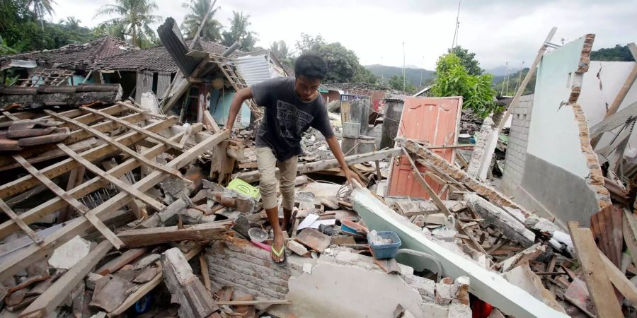 Ein Mann geht über die Trümmer eines vom Erdbeben zerstörten Hauses auf Lombok (IND).