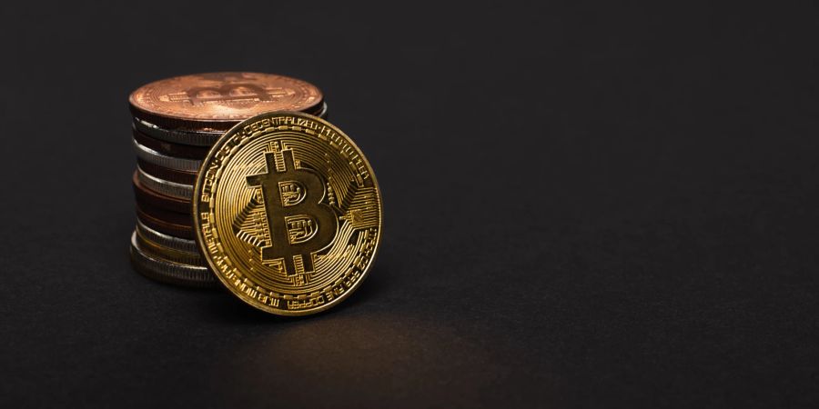 Physische Abbildung von Bitcoins auf einem schwarzen Tisch gestapelt