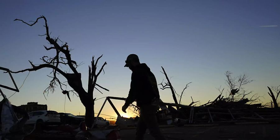 Ein Aufräumarbeiter geht am Ende des Tages an beschädigten Bäumen und Trümmern in Mayfield im US-Bundesstaat Kentucky vorbei. Foto: Mark Humphrey/AP/dpa