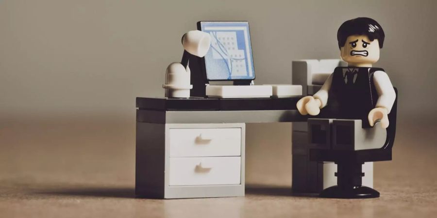 Lego Mann sitzt an einem Schreibtisch mit Computer und Lampe.