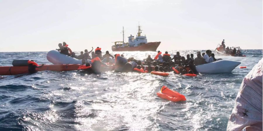 Zahlreiche Flüchtlinge, die auf Booten von Libyen aus nach Italien übersetzen wollten, werden während eines Rettungseinsatzes vor der libyschen Küste geborgen. Im Hintergrund das Rettungsschiff Aquarius.