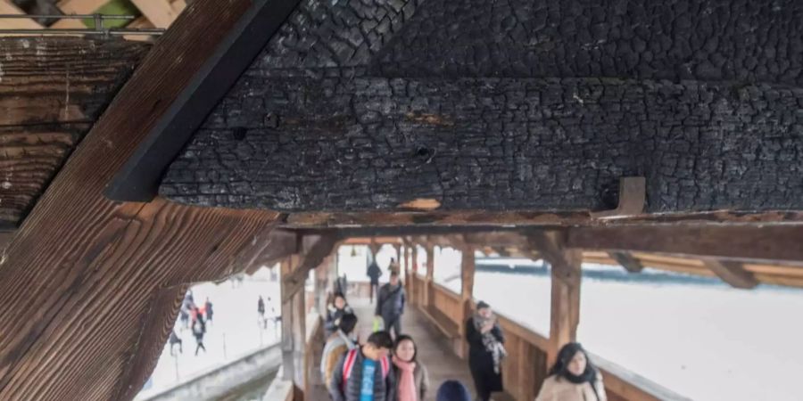 Ein versengtes, vom Kapellbrückenbrand gezeichnetes Originalbild hängt bei einem der zwei Eingangsbereiche der Brücke. Ein grosser Teil der Bilderrahmen sind seit dem Wiederaufbau der Kapellbrücke leer und werden nicht durch Kopien ersetzt. Foto vom 21. Februar 2018.