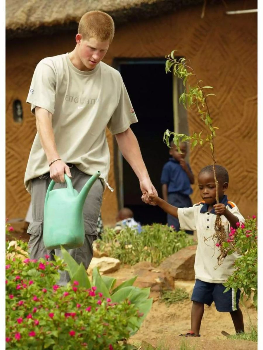 Prinz Harry giesst 2003 mit einem 4-jährigen Mädchen die Pflanzen vor einem Haus eines Kinderdorfes in Maseru, Südafrika.