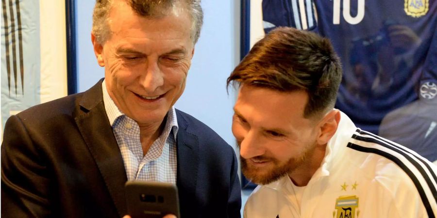 Mauricio Macri zeigt Lionel Messi etwas auf seinem Smartphone.