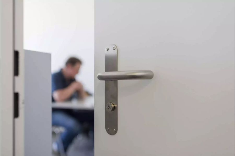 Unscharfer Mann an einem Tisch hinter einer scharfen weissen Tür - Keystone