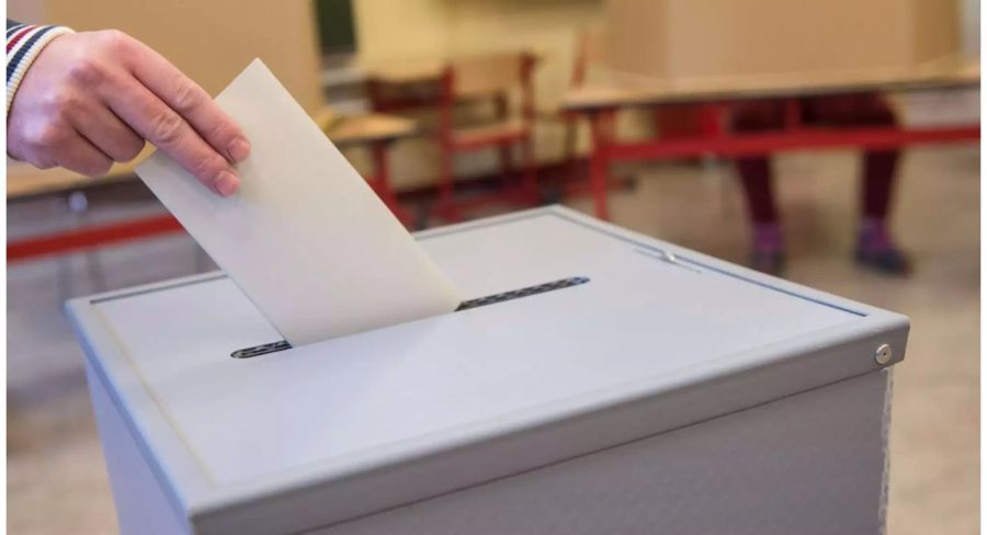 Hand wird Umschlag in eine Wahlurne - Keystone