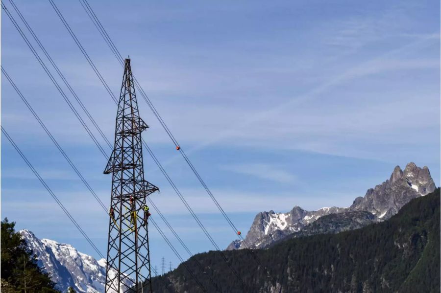 Starkstromleitung mit Arbeitern darauf und Bergen dahinter - Keystone