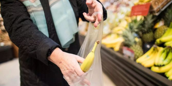 Eine Frau legt in einem Supermarkt eine lose Banane in eine Plastiktüte.