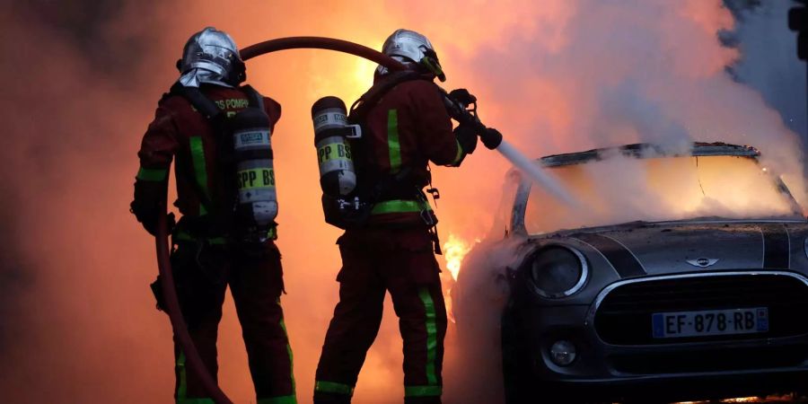 Feuerwehrleute löschen bei einem Protest der sogenannten «Gelbwesten» ein brennendes Auto.