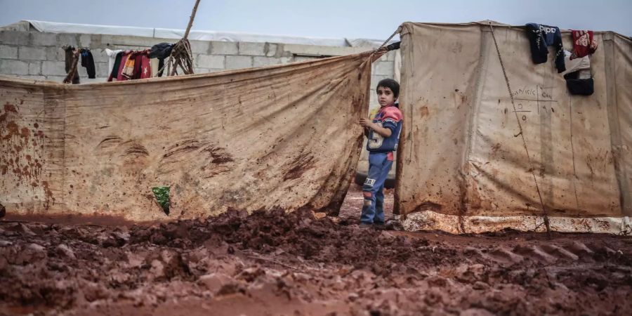 Ein vertriebener syrischer Junge steht bei Regenwetter im Schlamm in einem Lager für syrische Vertriebene.