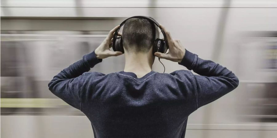 Ein Mann hört vor der U-Bahn Musik mit einem Kopfhörer.