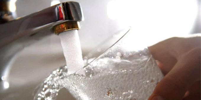 Ein Mann hält ein Glas unter einen laufenden Wasserhahn. wasser